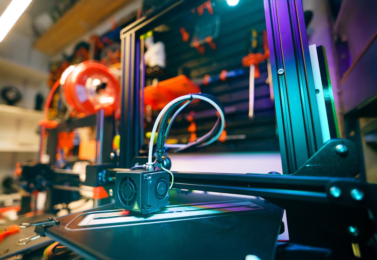 Close-up of a 3D printer actively printing inside a colorfully lit maker workshop