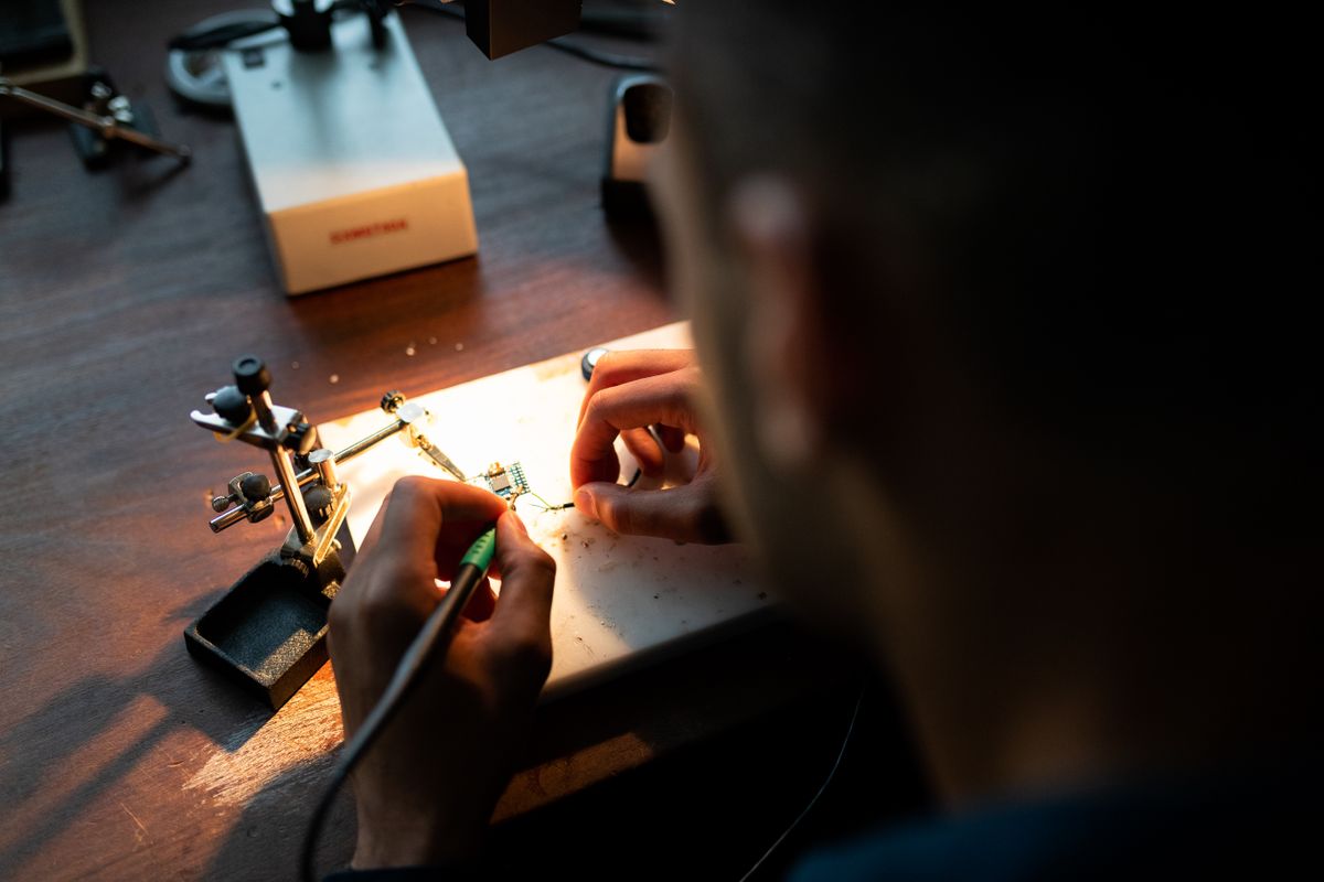 Maker soldering a circuit board prototype under a magnifying lamp on a workbench