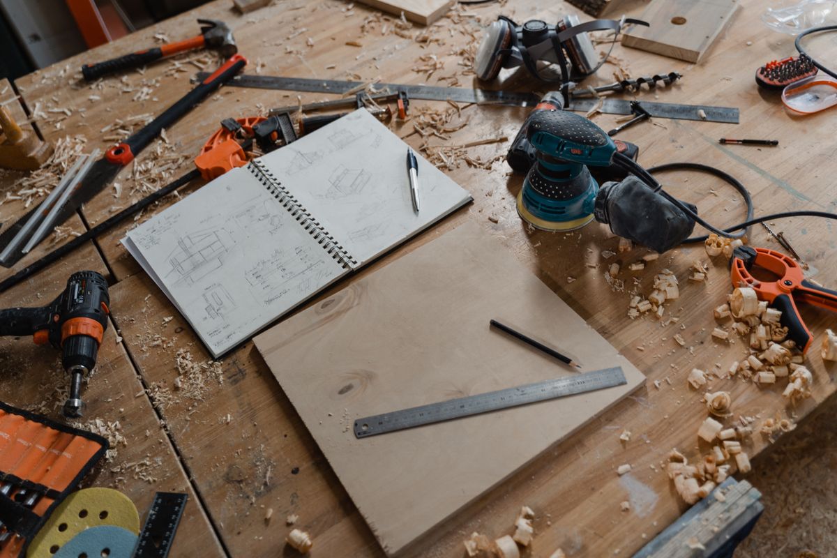 Workbench covered in hand tools, sawdust, and a sketchbook of build plans for a woodworking project